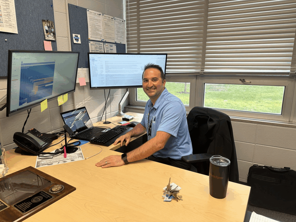 Athletic Director sitting at his office desk with multiple monitors, representing the professional environment of Athletic Director jobs.